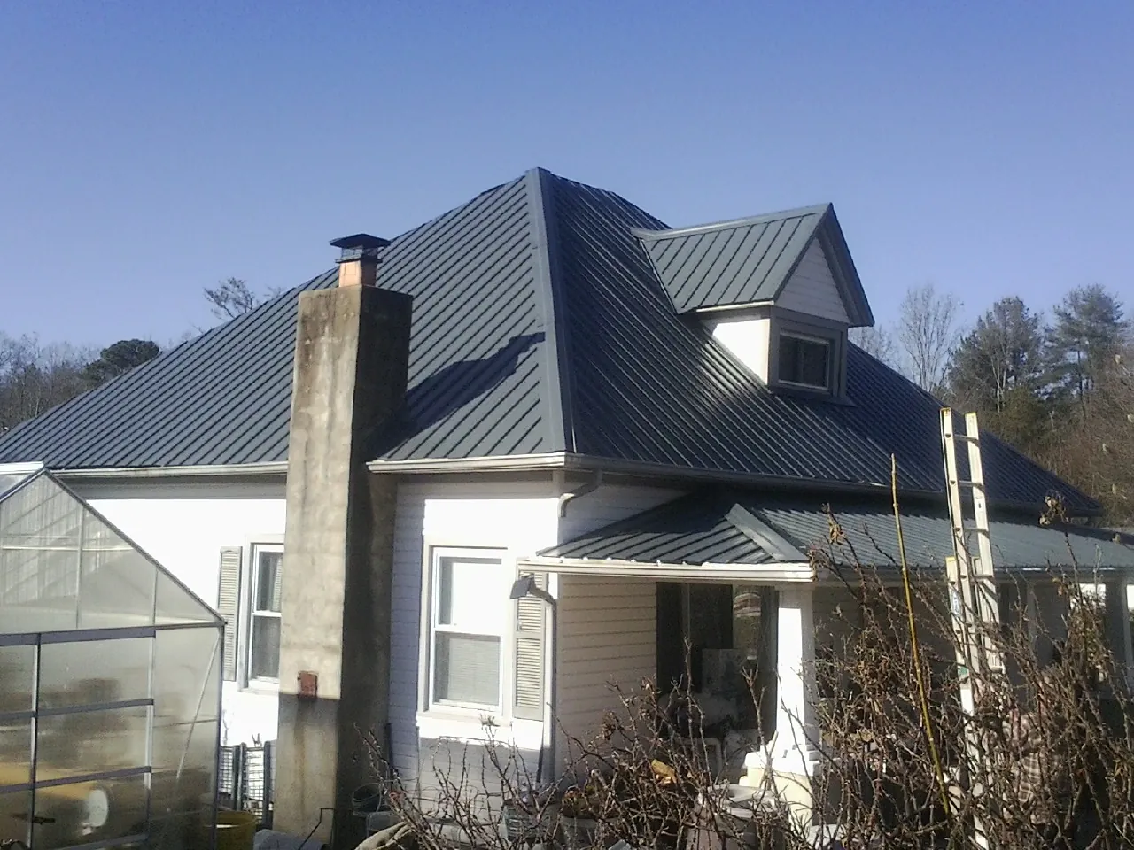 Dark blue standing seam metal roof on a white farmhouse with dormer — Slate & Tile Roof Repair by Roofing Brothers in Coolidge