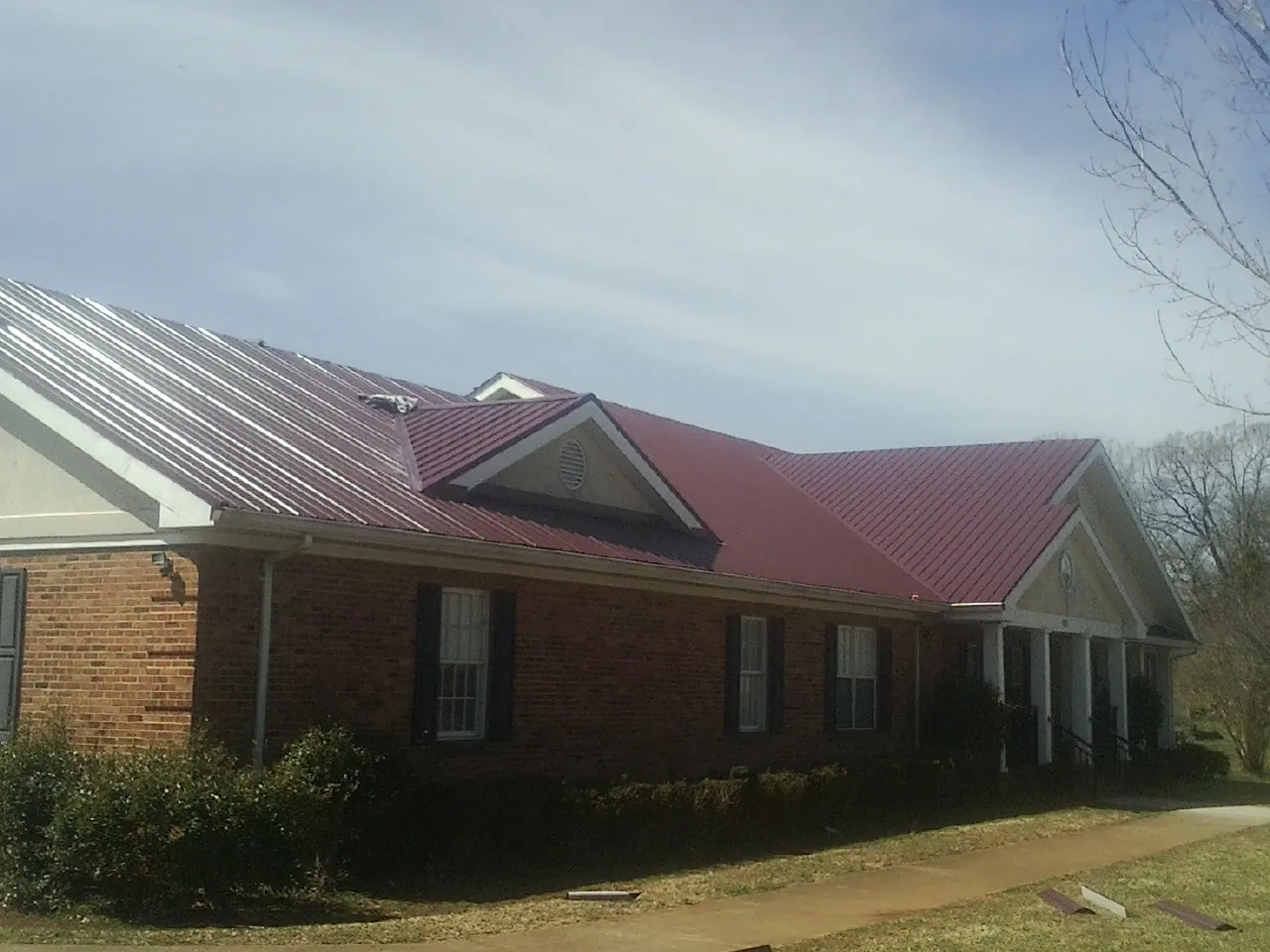 Red metal roof with gabled entries on a long brick building, from a Hail Damage Roof Repair job in Coolidge