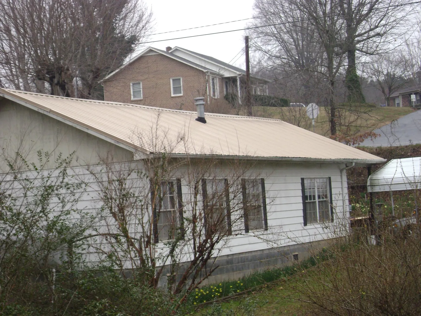 Tan metal roof on a white sided house set into a hillside — Commercial Roofing by Roofing Brothers in Coolidge
